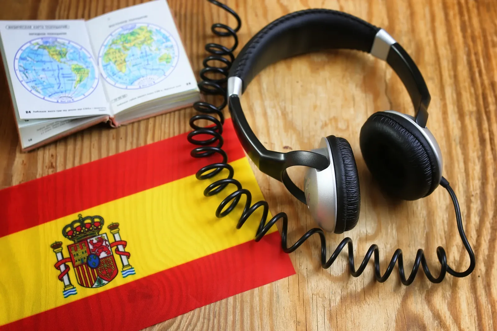 Traduction assermentée espagnol-français : drapeau espagnol, casque audio et atlas ouvert sur une table en bois